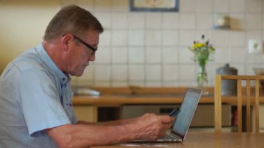 Emekli mutfakta oturuyor ve onun hesapları bir internet ve bir dizüstü bilgisayar kullanarak tarama. Masanın yanındaki banka kartları, bulunan el tutar bir cep telefonu mans. O gülümser ve onun yayılır