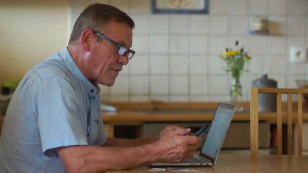 Сучасні технології та люди старшого покоління. Пенсіонер використовує ноутбук і телефон для оплати рахунків. Інтернет-банкінг, інтернет-магазин — стокове відео