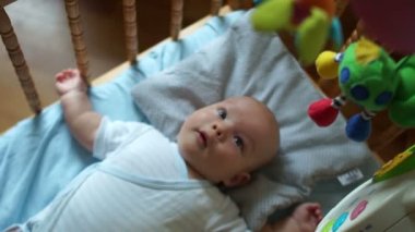 Yeni doğan mobile ile mavi yatak ve oyuncaklar yatıyor. Çocuk aktif oyuncak için tepki verir, kalemler ve bacaklarını çeker