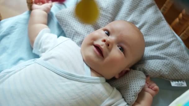 Um bebé de três meses está deitado na cama. Uma criança olha para cima e sorri. Ele está ativo, puxando as mãos e pernas, abre a boca, olha de perto — Vídeo de Stock