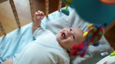 Çocuk sevinçle yeni oyuncak için tepki verir. Bebek beşik içinde hareket eden. Çocuk oyuncak, hamle, gülümsüyor gözleri izler ve ağız açılır