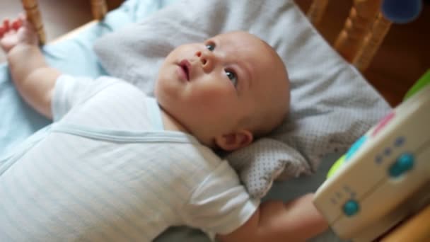 Un niño de tres meses está muy contento con el nuevo juguete. El niño se ríe, tira de sus piernas y mira sus ojos móviles — Vídeos de Stock