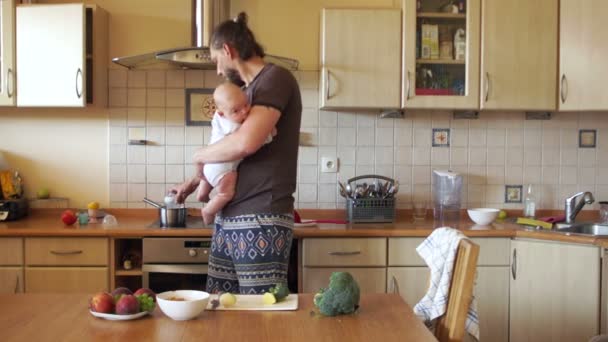 Multitasking jonge moderne vader. Wanneer moeder niet thuis is. Een man probeert om een maaltijd te koken zal het trekken van de baby. Fathers Day. Versnelde video afspelen — Stockvideo