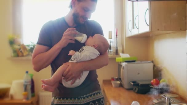 Padre sosteniendo y cuidando a un bebé pequeño, alimentándose del biberón. Un padre solitario en la cocina. Día del Padre — Vídeos de Stock