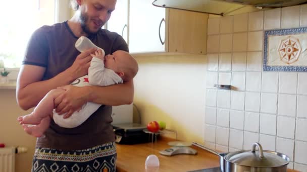 The baby is in the hands of his father. Dad feeds the baby. My father is preparing to eat in the kitchen. Fathers Day — Stock Video