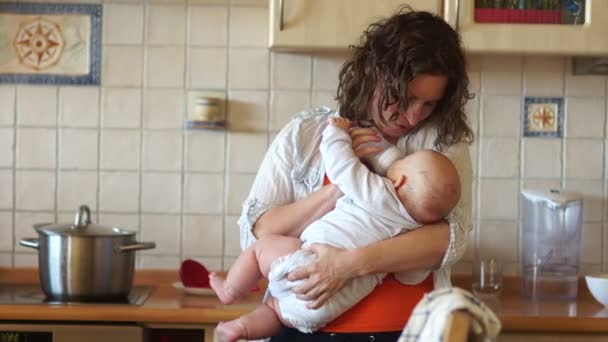 Mamãe alimenta seu bebê de uma mamadeira, de pé na cozinha perto do fogão. Dona de casa, licença de maternidade. Alimentos para bebés — Vídeo de Stock
