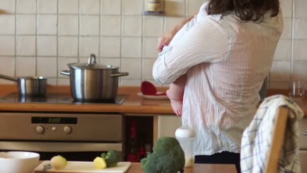 La donna finisce di nutrire il suo bambino dal biberon. Prende un mestolo e mescola la zuppa bollente sul fornello. Festa della mamma, casalinga — Video Stock
