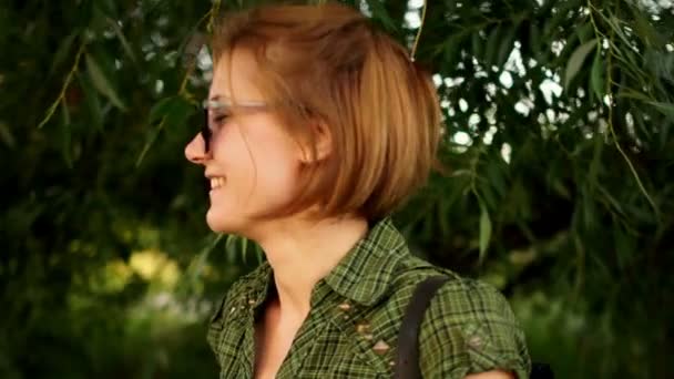 Vidéo dynamique. Portrait en gros plan d'une fille aux cheveux roux portant des lunettes de soleil sur fond de verdure estivale. Beauté naturelle, vacances d'été, journée ensoleillée — Video