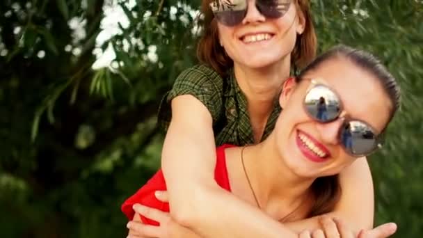 Два прекрасных студента отдыхают в парке на летних каникулах. Девушки носят солнечные очки. Кемпинг, путешествия, свободные отношения — стоковое видео