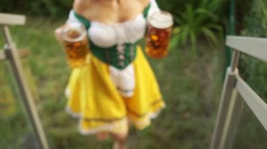Oktoberfest garson iki büyük bardak bira taşır. Kız çıplak ayakla çimlerde yürüyor ve merdivenlerden tırmanıyor. Bavyera geleneksel kostüm, seksi dekolte
