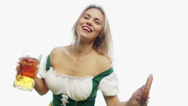 Девушка в традиционной баварской трахте пьет пиво из огромной кружки, держа крендель в другой руке — стоковое видео