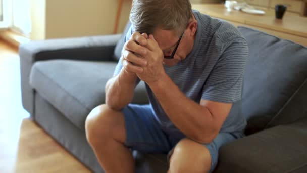 An elderly man in depression is sitting on the couch. He lowered his head, the problems of pensioners — Stock Video