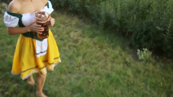Mooie blonde serveerster op het muziekfestival Oktoberfest in Duitsland. Een meisje in een Beierse pak wandelingen van het gras en bier aan klanten draagt — Stockvideo