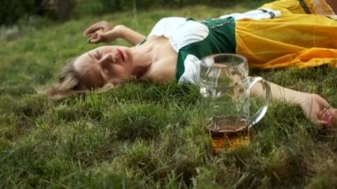 Asosyal davranış, aşırı içme. Bir boş bira cam yanındaki çimlerde Ulusal Bavyera kostümlü bir kadın yatıyor. Yakın çekim. Festivali Oktoberfest