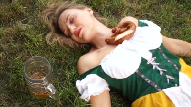 Alkol zehirlenmesi. Bir geleneksel Bavyera içinde bir güzel sarhoş genç kadın yerde yatıyor. Müzik Festivali oktoberfest. Yakın boş bir bardak bira ve cips standları — Stok video