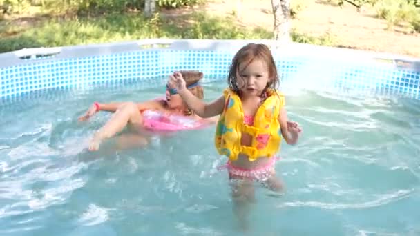 Dos hermanas nadan en una pequeña piscina inflable. Verano en el pueblo. Feliz familia, felices fiestas — Vídeos de Stock