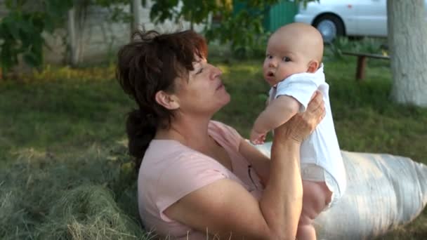 Dojrzałe mama posiada swojego syna w ramionach. Dzieciak wygląda zaskoczony. Kobieta i dziecko siedzi z ogrodem na trawie. Sztuczne zapłodnienie, Ivf — Wideo stockowe