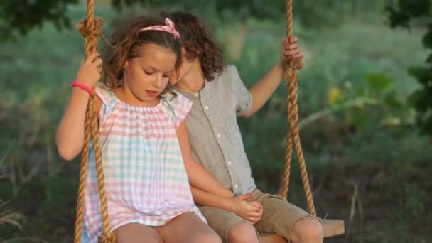 Children in love couple riding on a seesaw holding hands. A boy and a girl whisper to each other in the ear and laugh happily. Summer vacation — Stock Video