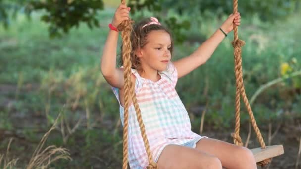 Young love between boy and girl on romantic summer evening. Couple of happy kids hugging and swinging on wooden swing at golden sunset. Brother embracing little sister on a swing — Stock Video