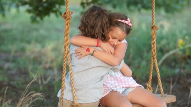 Hermano abrazando a hermanita en un columpio. Joven amor entre chico y chica en la romántica noche de verano — Vídeos de Stock