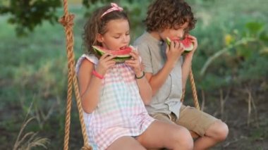 Öğrenciler tatil. Çocuklar bir salıncak üzerinde oturan karpuz yemek. Kız tohumları tükürür