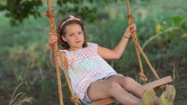 Ein Schulmädchen reitet fröhlich auf einer Schaukel. Frohe Sommerferien. braunäugiges, gelocktes Mädchen — Stockvideo