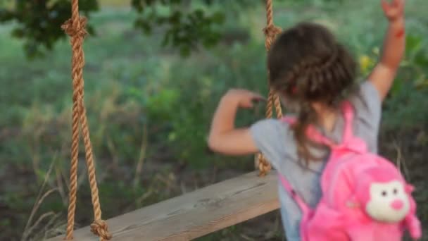 A little girl with a backpack on her back came to ride one on a swing. Summer holidays — Stock Video