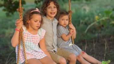 Üç çocuk bir salıncağa binmek. Büyük çocuk bebeğe bir şey söylüyor ve o kaçtı. Mutlu aile, yaz tatili