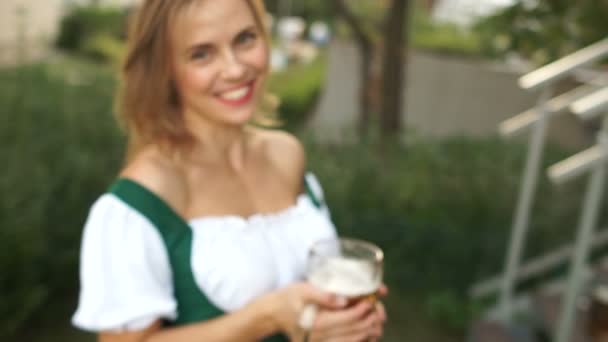 O chelneriță fermecătoare ține un pahar de bere rece spumoasă lângă decolletă. De aproape. Festivalul Berii Oktoberfest — Videoclip de stoc