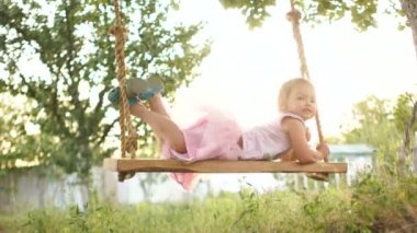 Harika bir bebek büyük ev yapımı salıncakta yatıyor. Bir çocuk kabarık pembe etek, bahçedeki bir salıncak üzerinde bir Bale tutu rides