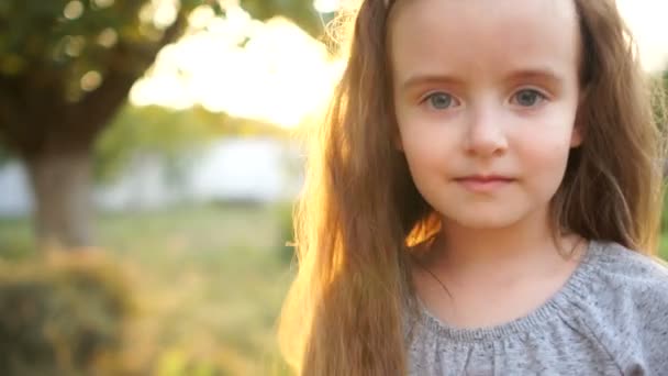 Ett nära porträtt av en ledsen liten flicka med långt hår och stora grå ögon. Barnet är generad, blyg och ledsen. Vinden blinkar med hennes lockar — Stockvideo