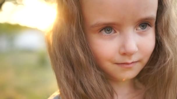 A long-haired little girl looks at the frame with big gray eyes. Close portrait, natural beauty, little beauty — Stock Video