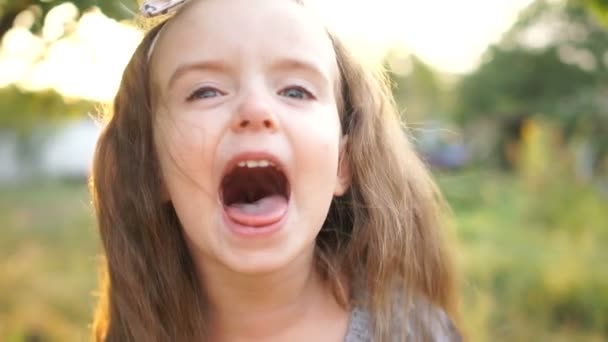 Una niña con el pelo largo grita de alegría. Junto a ella, su amiga escupe y muestra su lengua. los niños tontean. Todos los tontos día — Vídeo de stock