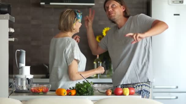 A mature woman and a young man are dancing in the kitchen. A couple with an age difference, the mother prepares dinner for her adult son — Stock Video