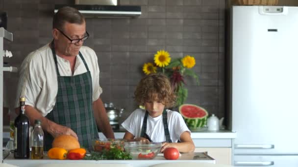 Un ragazzo taglia un cetriolo per un'insalata. Un uomo maturo lo loda. Cucina moderna. nonno insegna a suo nipote a cucinare. Cucina vegetariana — Video Stock