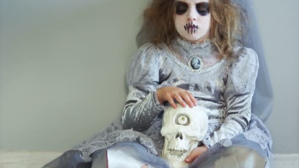 Kız öğrenci bir gri cadı kostümü ile bir çelenk başında oturur ve tek gözlü bir kafatası onu kucağına tutar. Sıradışı Cadılar Bayramı yaratıcı, ölüler günü ' — Stok video
