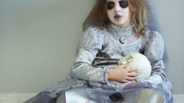 彼女の頭に花輪を捧げると灰色の魔女衣装メイクで女の子ティーンエイ ジャーは、座っているし、膝の上に 1 つ目の頭蓋骨を保持しています。死者の型破りなハロウィーン、創造的な日 — ストック動画
