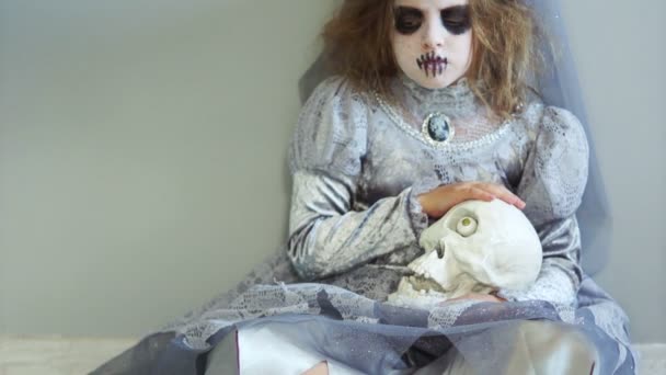 Un niño en el maquillaje y el traje de la novia de Drácula celebra Halloween. Chica sosteniendo un cráneo. Suspirando y triste, mirando a la cámara — Vídeo de stock