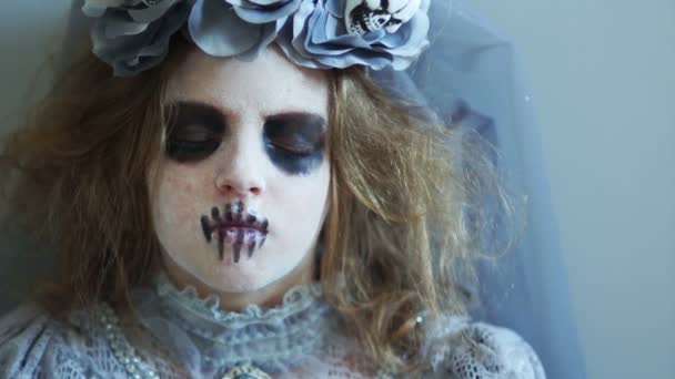 Horreur, un enfant maquillé dans un cadavre ouvre soudain les yeux. Un portrait serré d'une fille en costume visite dracula, Halloween. Approche créative des vacances. Gris, palette de couleurs froides — Video