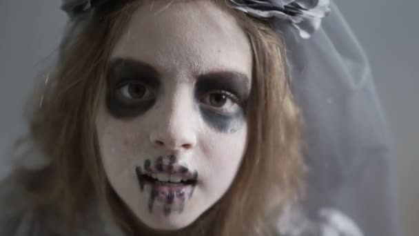 I bambini festeggiano Halloween. Una ragazza nel trucco di un morto e nel costume della sposa di Dracula, un ritratto ravvicinato. Una corona di teschi e veli grigi. Tavolozza fredda per Halloween — Video Stock