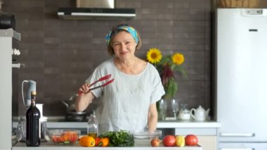 Olgun kadın onun mutfak yemekleri için kırmızı bir spatula ile dans. Masada, büyük ruh, modern mutfak iç, parlak sebze yemek