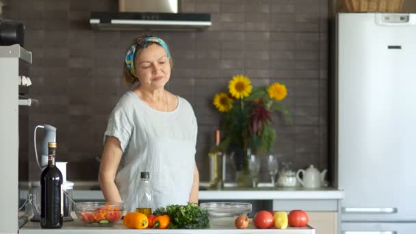 Mujer madura y su hijo adulto en la cocina. Ella baila, él viene y le da una rosa amarilla. Se ríen juntos y siguen bailando. Día de las Madres — Vídeo de stock