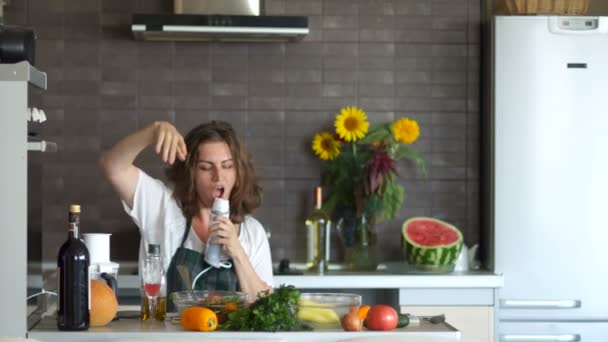 Ibu rumah tangga muda yang seksi menari di dapur dan bernyanyi dalam mixer. Seorang wanita dalam suasana hati yang besar mempersiapkan salad. Makanan sehat, keluarga bahagia, hari ibu — Stok Video