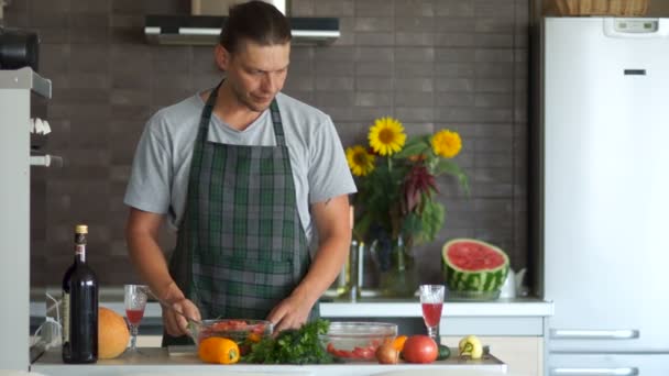 Een man in een schort in de keuken. De kerel is gek rond met een ernstig gezicht. Worpen peper zoals een granaat. Verbergen onder de tafel — Stockvideo