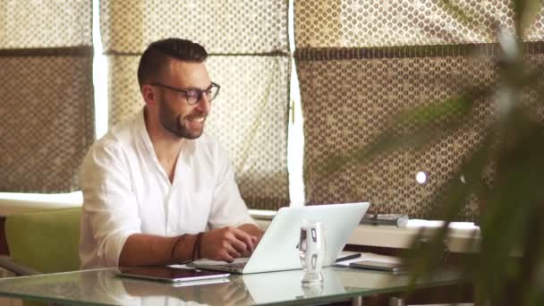 Joyeux bel homme d'affaires au travail dans le bureau. Souriant regarde dans le cadre. Il porte une chemise blanche, une barbe et des lunettes — Video