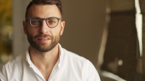 Handsome businessman in glasses looking at camera. A man in a white shirt smiles, puts on his glasses. Lucky businessman, office employee, financier — Stock Video