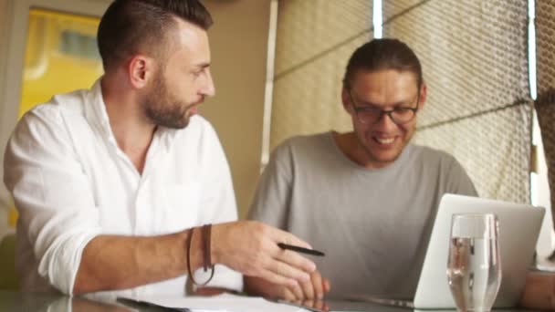 Kollegen besprechen den Businessplan. Mann in weißem Hemd und Bart streitet mit einem Mann in T-Shirt und Brille. Lächeln, Konsensbildung, gegenseitiges Verständnis, Unternehmensethik — Stockvideo