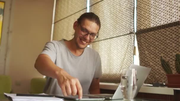 Joven hombre de mente guapo en jeans camisa y gafas sentado en la mesa y typink una carta a su conocido. Freelancer trabaja en casa, quita gafas y suspiros de alivio. Fin de la jornada laboral — Vídeo de stock