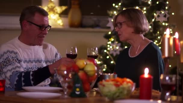 Зрелые муж и жена пьют красное вино из своих стаканов, сидя за крытым столом со свечами. Мужчина и женщина целуются. С Рождеством, День Благодарения. — стоковое видео