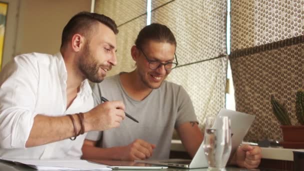 Spotkanie w coworking. Dwa freelancerów omówić projekt w pobliżu laptopa i tabletu. Wnętrze na brązowe odcienie — Wideo stockowe
